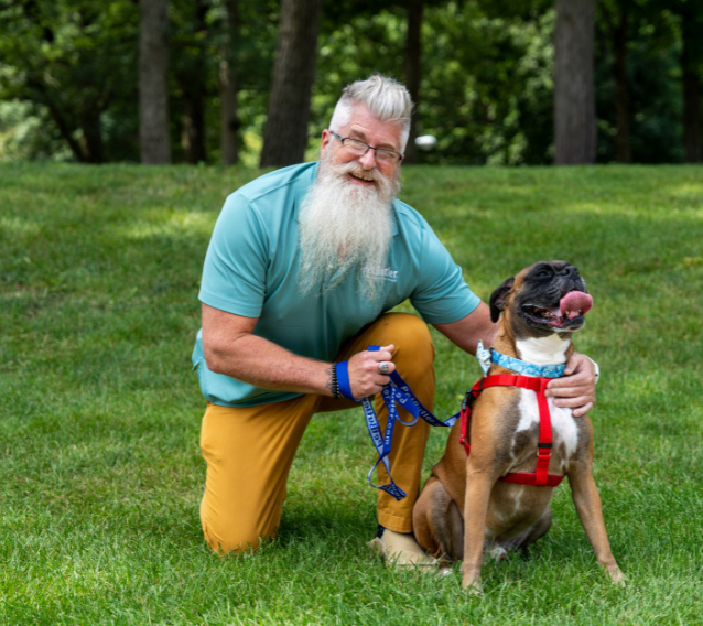 Bryan Peirce, Manager of Pet Butler Columbus OH sitting with a boxer dog breed on a green lawn on a sunny day. Dog Walking - Pet Sitting - Pet Sitter - Pet Care Services - Dog Walker