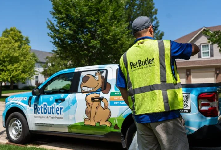 Pet Butler professional in a yellow logoed vest removing an item from the back of a Pet Butler pick up truck.