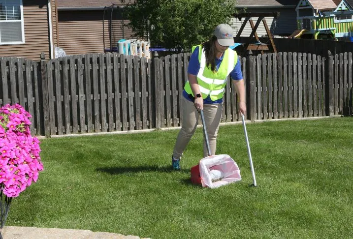 Pet Butler professional using a rake and bucket to remove pet waste from a backyard.