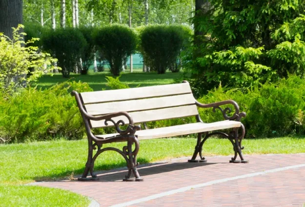 Empty wood and metal bench on a paver pathway in front of lush green landscape.