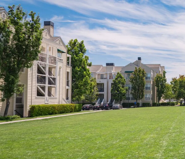 Beige, low-rise, multi-family buildings next to large open grassy area.