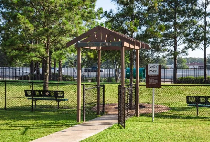 A sidewalk leading to a gated dog park with wood roofed structure and two benches at the entry.