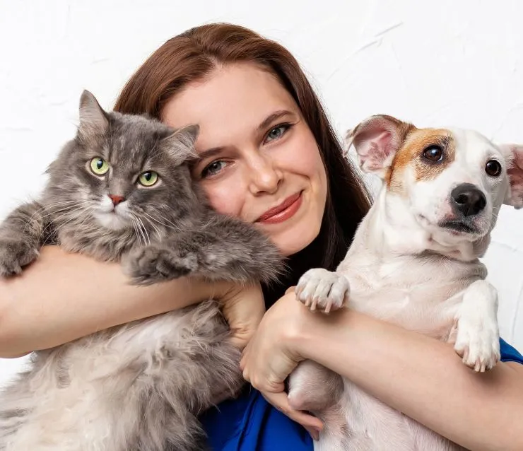 Female Pet Butler pet care professional hugging a grey cat and small white dog to her face.