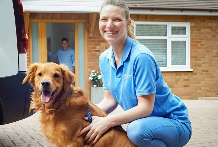 Pet Butler pet care professional in a blue polo shirt kneeling next to a Golden Retriever dog on a driveway.