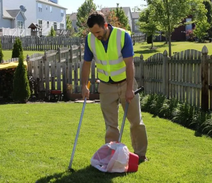 Pet Butler poop scooping professional removing pet waste from a backyard using a rake and a bucket.